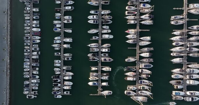 Top down aerial view of a marina at sunset, showing boats and yachts neatly moored in parallel rows.