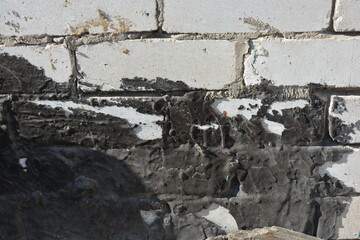 Construction and renovation work, a building wall with a thick black layer of resin, flaws, and unevenness, the first masonry. A wall of white brick, gray cement, illuminated by the rays of the sun.