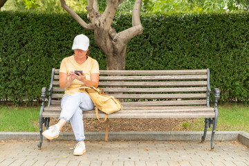 Woman using smartphone while sitting on a bench in a park during daytime surrounded by greenery