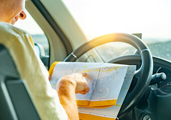 Driver studying a map while preparing for a road trip at sunset over a scenic landscape
