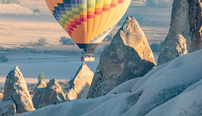 Colorful hot air balloon floats over rocky landscape in Cappadocia during sunrise