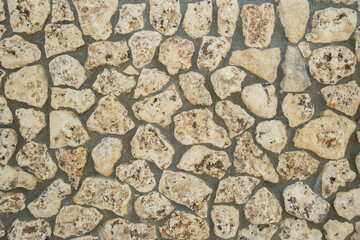 Natural stone wall with various shades and textures creating a rustic appearance in a sunny outdoor setting