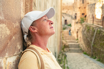 Woman rests against a stone wall while exploring an ancient village in warm afternoon light