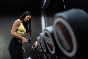 Smiling female professional gym trainee exercising with dumbbell weights.