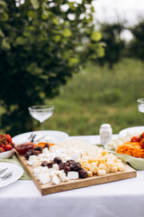 Cheese platter on outdoor picnic table with fruits, toast, and wildflowers.