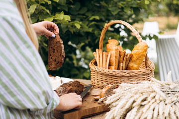 Female hands slicing fresh bread and spreading butter at outdoor garden picnic.