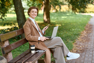 Obraz premium Young man enjoys autumn outdoors while working on laptop in stylish coat