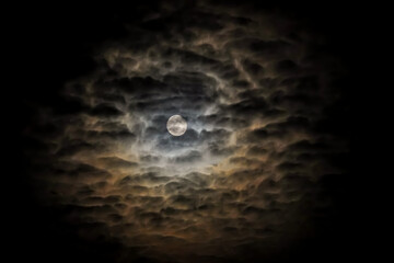 Full moon on a dark cloudy night with clouds flying in front of the moon like in thrillers and horror movies. Dark night sky, black clouds. Real shooting