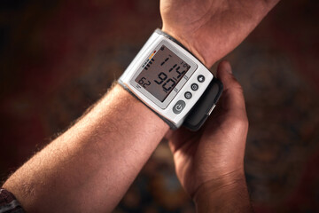 Man checking blood pressure and heart rate at home with a portable modern digital meter.
