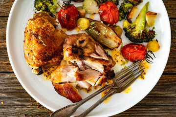 Roasted chicken thighs with grilled vegetables on wooden table. Top view