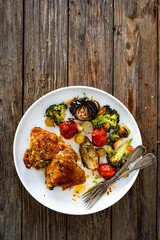 Roasted chicken thighs with grilled vegetables on wooden table. Top view