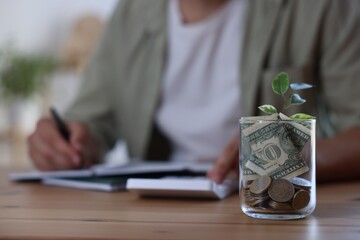Glass jar with money and seedling. Man budgeting at desk, selective focus
