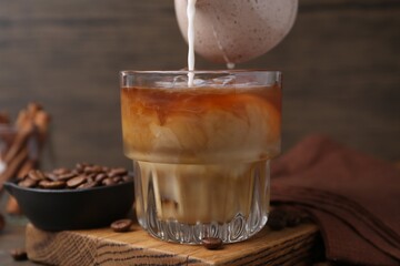 Pouring milk into iced coffee at wooden table, closeup