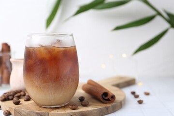 Tasty iced coffee in glass and beans on white tiled table, closeup. Space for text