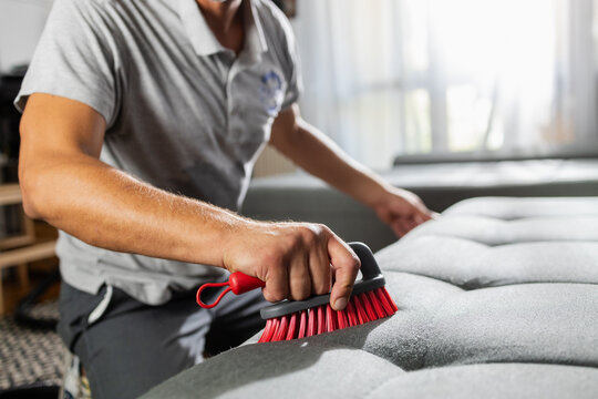 Man cleaning gray sofa with upholstery brush