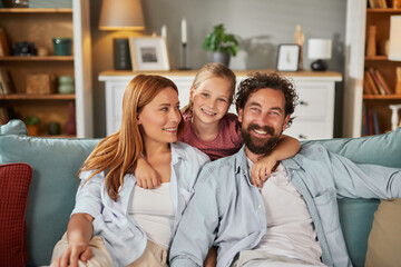 A happy family with a smiling girl is spending time together in a cozy living room filled with warmth and love. The parents are seated comfortably on a couch.