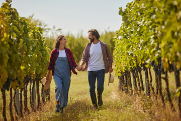 A couple strolls hand in hand through a lush vineyard, sharing laughter and joy amidst rows of grapevines during a sunny afternoon in harvest season.
