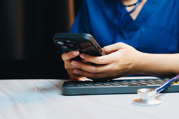 Telemedicine concept. Medical Professional Using Smartphone While Sitting at Desk with Keyboard and Stethoscope in Modern Office Environment