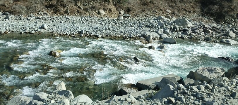 Close-up of Rapid Turquoise River Water Flowing Over Grey Boulders and Rocks