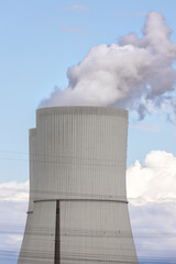 Tall cooling tower releasing steam into blue sky, symbol industrial energy production and technology. The structure represents power generation, heat emission and environmental engineering in Germany