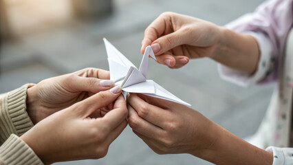 Teamwork concept shown by two people holding white paper origami crane together symbolizing cooperation and unity in creative way