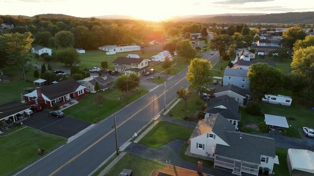 Beautiful aerial view of a small American town at sunset. Golden hour lights glows over quiet suburban streets, cozy houses and lush green trees. Peaceful and picturesque scene of rural American city.