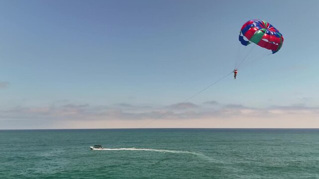 Side drone shot capturing parasailing in Monta&ntilde;ita, Ecuador. A person glides above the open Pacific Ocean, with boats pulling the colorful parachute across the water.