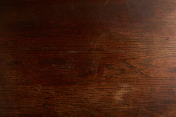 Dark rich brown wooden texture background with visible grain and subtle scratches, resembling an antique mahogany or walnut surface.