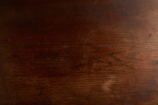 Dark rich brown wooden texture background with visible grain and subtle scratches, resembling an antique mahogany or walnut surface.