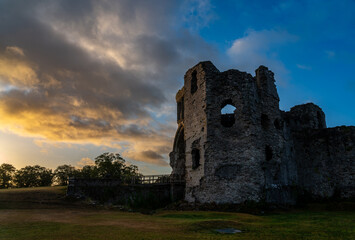Early morning light over the ancient stone ruins of Denbigh Castle with dramatic clouds and warm sunlight breaking through at sunrise