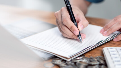 Personal finance planning and savings calculation at home , Close-up of a person writing in a notebook a calculator and stacked coins, representing personal finance planning, savings management.