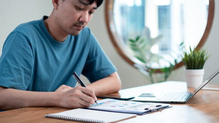 Man analyzing financial chart and taking business notes, representing business strategy, financial analysis, investment planning, and personal finance management at home office.