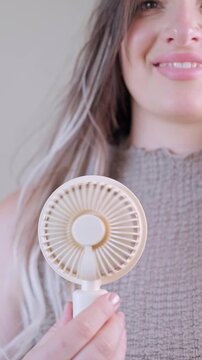 Summer gadget concept young woman enjoying cool air from her mini fan outdoors on a warm sunny day.