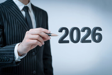 A businessman in a suit points with a pen towards the year 2026, symbolizing planning and future of business and innovation