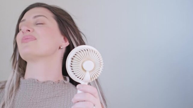 Young woman holding a compact fan feeling refreshed and cool outdoors on a hot sunny summer day.