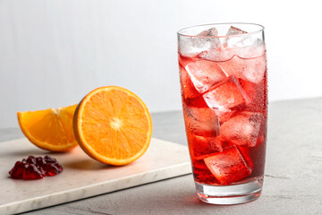 Highball glass with red cocktail ice cubes and orange slice on minimalist background
