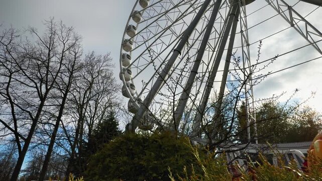 A striking low-angle, wide-view shot of a modern, large white Ferris wheel, its intricate metal structure and passenger cabins dominating the upper right frame. The scene is set against a bright