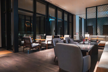 Contemporary hotel lounge in Japan, low armchairs and wood sofas around a dark coffee table, candles and flowers present, floor to ceiling windows, warm evening lighting.