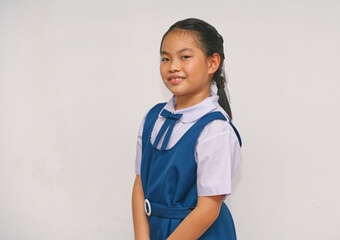 Asian child in a blue school uniform smiles confidently against a plain background. The image portrays education, youth, and positivity, ideal for themes related to learning and school life.