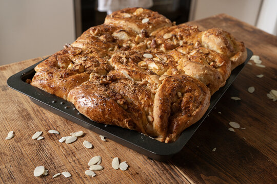 Freshly baked cinnamon roll cake with apple and almond topping in a baking tray on a rustic wooden table