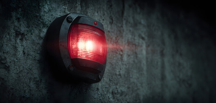 Red fire alarm strobe light flashes, emitting red beams in dark corridor. Audible alarm sounds in background. Security device is mounted on rough concrete wall, signaling emergency or system test.