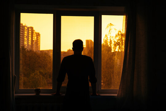 Man watching sunrise through window