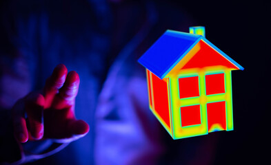 Naklejka na ściany i meble A hand touches a house model with a colorful heat map effect, illustrating home energy, concept of smart home