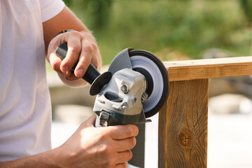 A man's hands sand a homemade wooden bench with a angle grinder outdoor. Close up. DIY