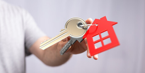 A hand presenting a house key and a red house-shaped charm, symbolizing home ownership, real...