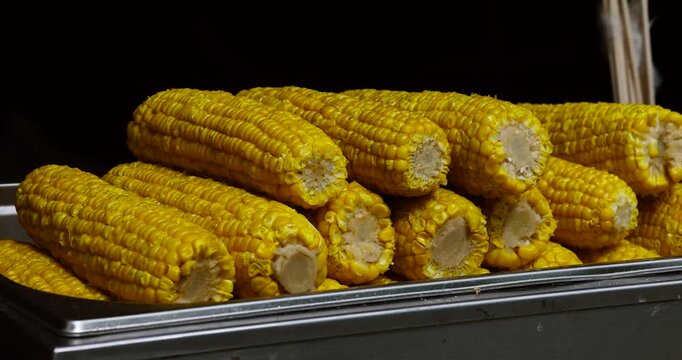 Fresh juicy boiled corn stacked in a pile at a summer market. Street food concept, fair snack, healthy and tasty treat.