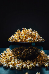 A large bowl of fresh buttered popcorn on a dark background with dramatic lighting and scattered pieces