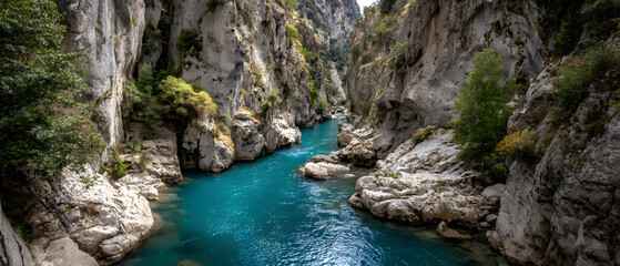 Obraz premium Vivid blue river carving its way through a rugged canyon framed by steep rocky walls.