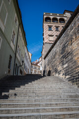 Stairs winding between buildings on a hill in Prague, Czech Republic, leading toward Prague Castle, photographed against a clear blue sky.
