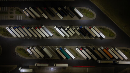 Aerial view of a truck stop at night, showcasing rows of parked semi-trucks in their designated...